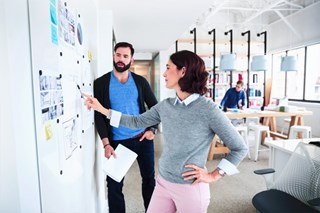Man and woman in front of a whiteboard full of posted papers and notes